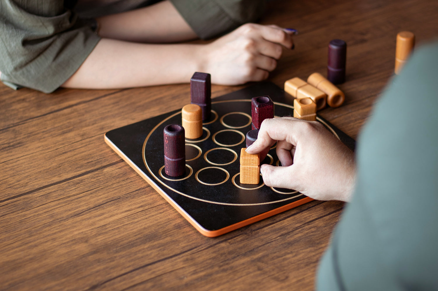 Partie de jeu de société en cours sur une table du Joker Pub Ludique, boîtes ouvertes et mains sur le plateau.